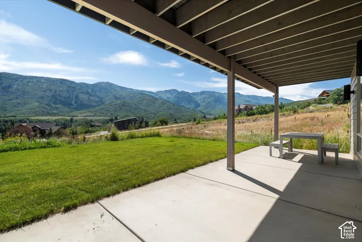 Covered outdoor patio with concrete flooring and exposed beam ceiling, opening onto a grassy lawn