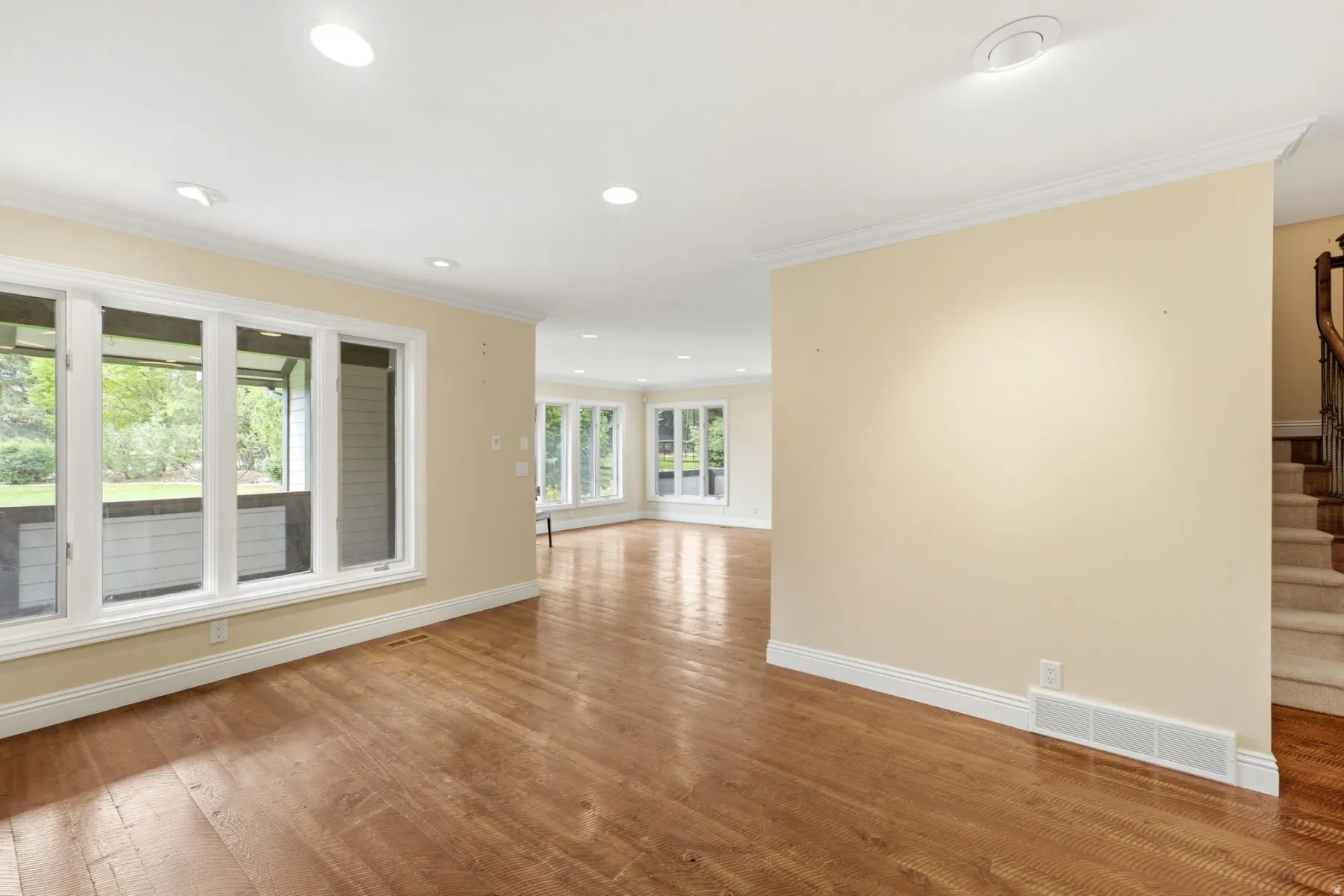 Hardwood flooring, recessed ceiling lighting, crown molding, multiple windows, and a carpeted staircase with wood railing