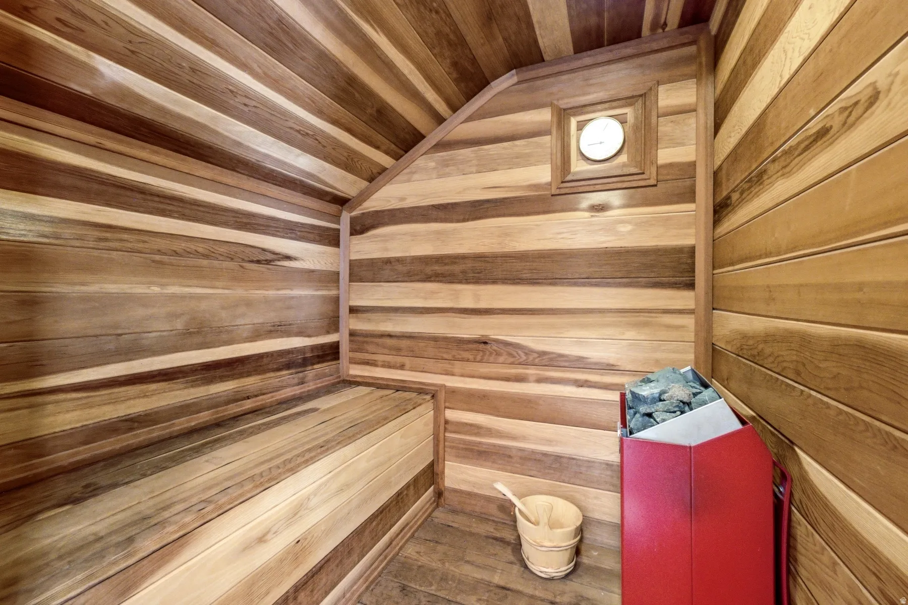 Wood-paneled sauna featuring built-in bench seating and a red sauna heater
