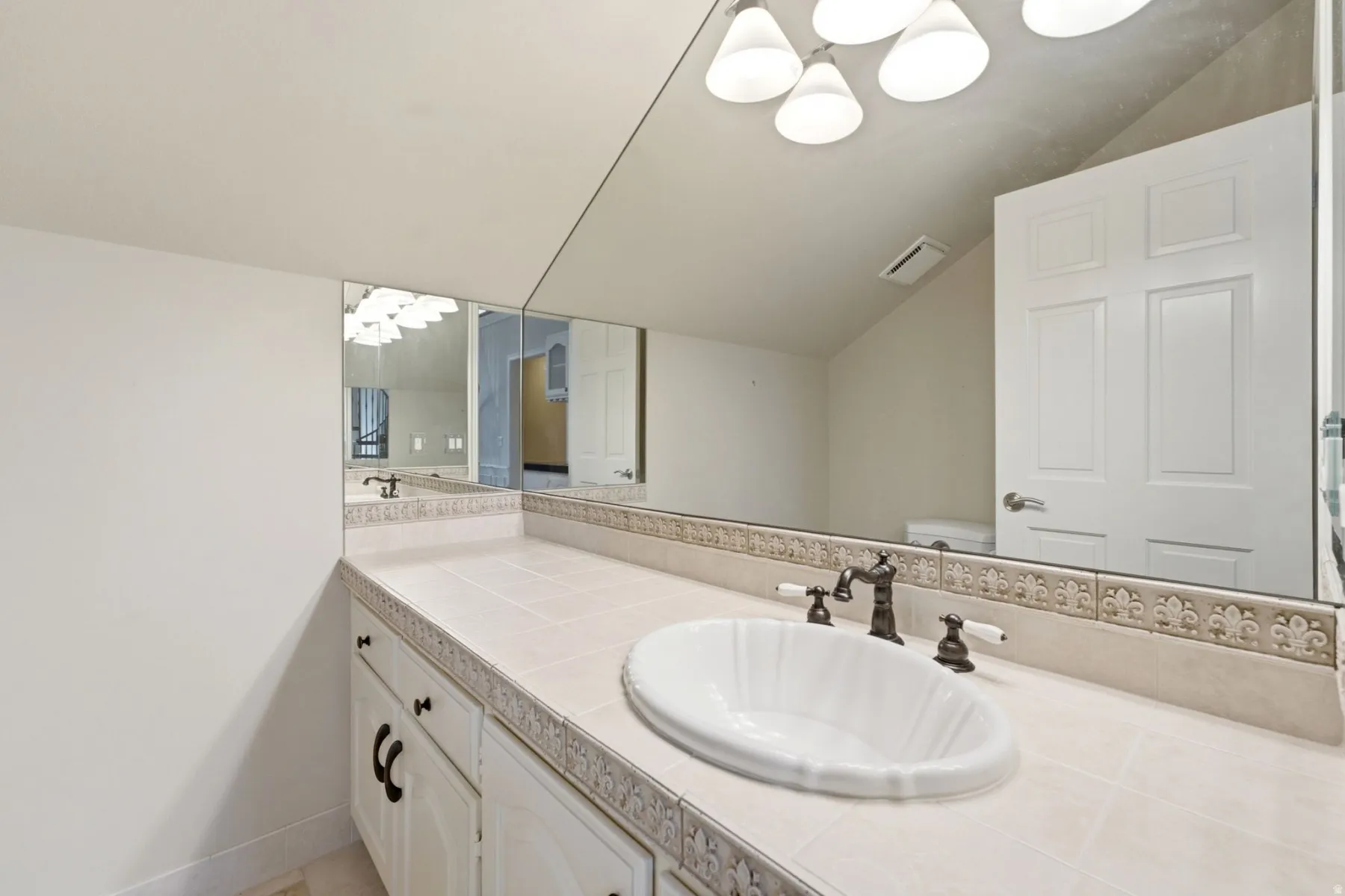 Spa-inspired bathroom vanity featuring dual sinks with white vessel basins, stone-finish countertops with decorative tile inlay, oil-rubbed bronze faucetry, and white cabinetry with hardware accents