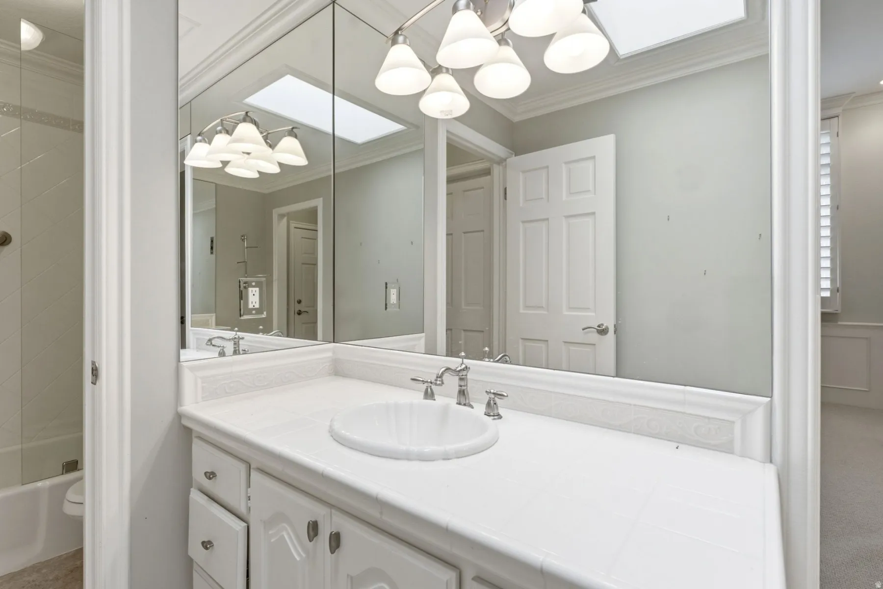 White vanity with integrated sink, chrome-finish faucet, mirror-front medicine cabinets, and overhead lighting