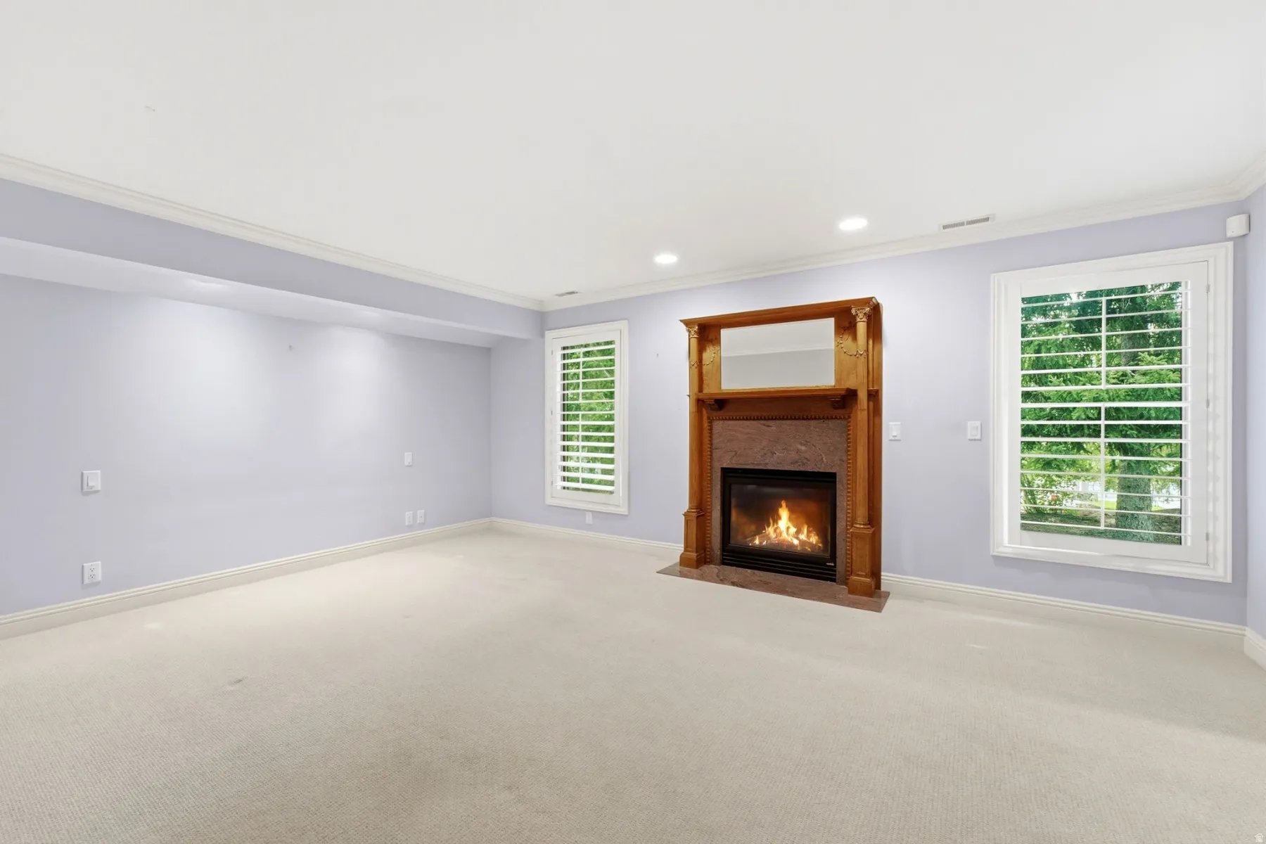 Recessed lighting, crown molding, a fireplace with a wood mantel, stone surround, and two windows with plantation shutters