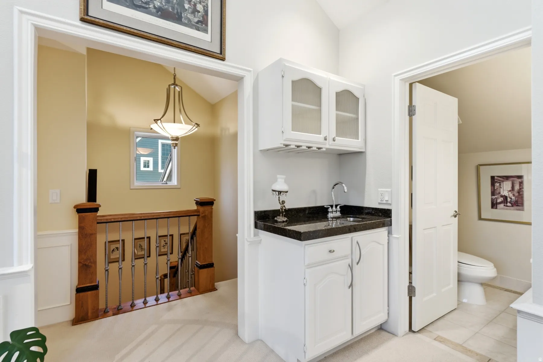 Built-in wet bar with white cabinetry and dark stone countertop, recessed sink with chrome faucet, and glass-front upper cabinets