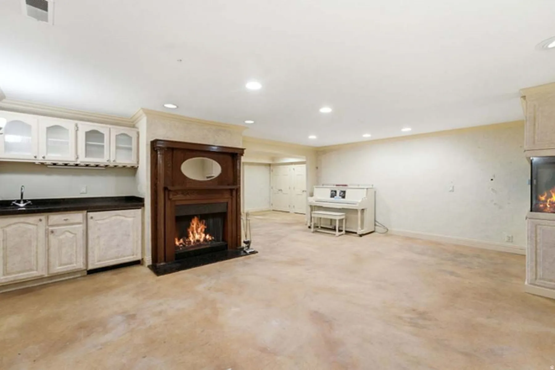 Built-in wet bar with white cabinetry and dark countertop, wood-mantle fireplace with dark surround, recessed lighting, and light-toned flooring