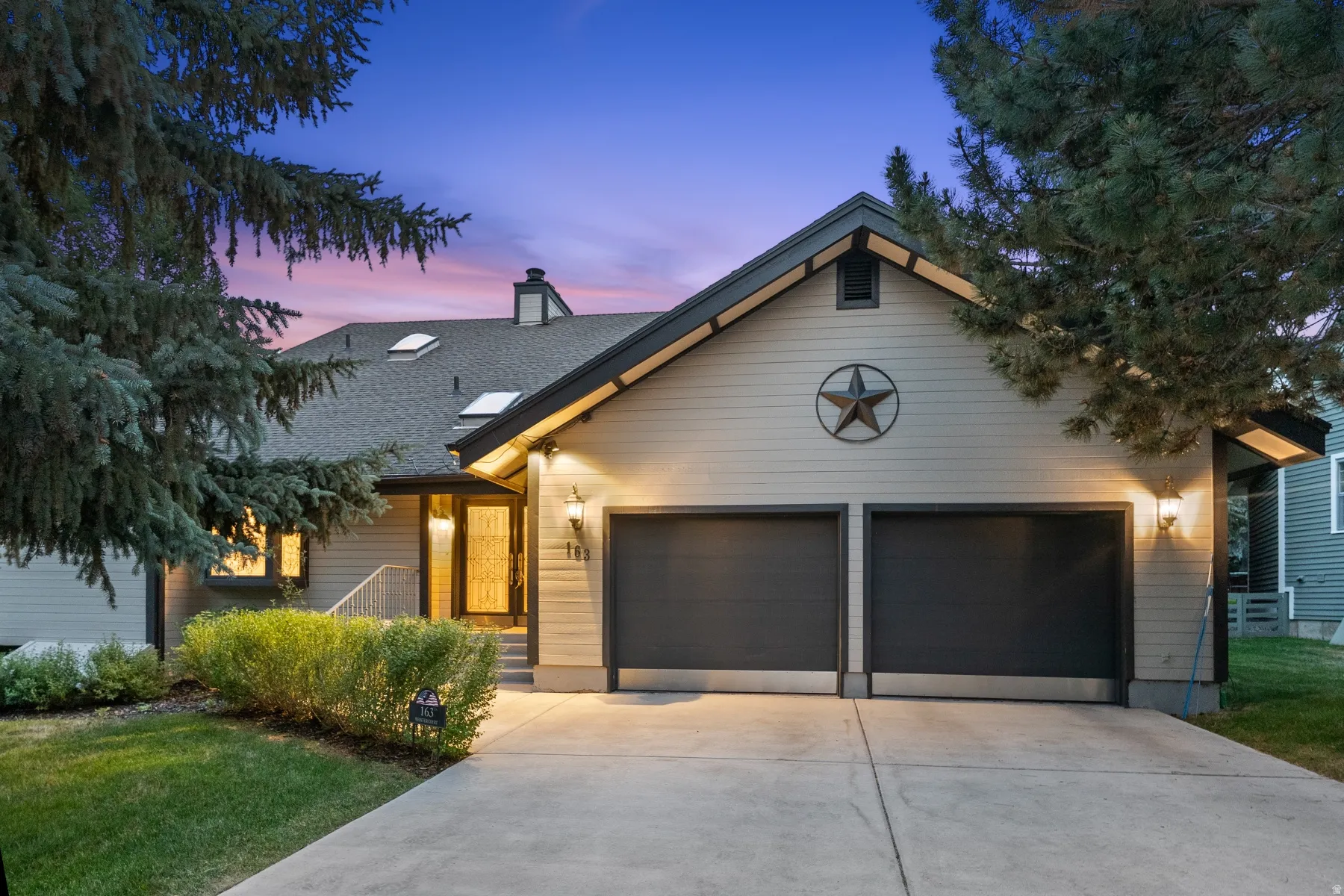 Exterior featuring two garage doors, prominent roofline with skylights, and a lighted entry