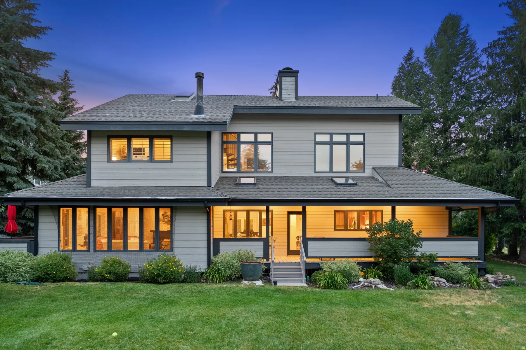 Modern siding exterior with a multi-level roofline, extensive windows, a covered porch, and mature landscaping
