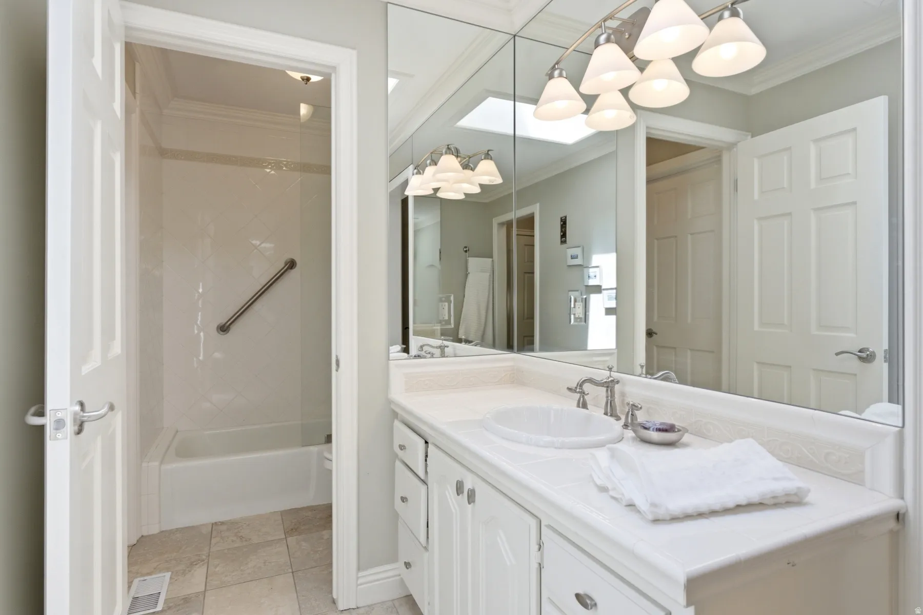Bathroom featuring a white vanity with an integrated sink, brushed nickel faucet, large wall mirror, and a white tub with tile surround
