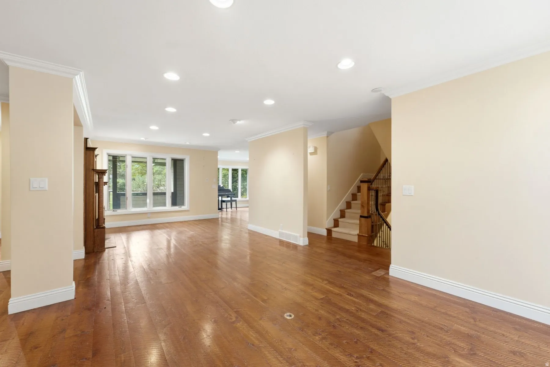 Hardwood flooring, recessed lighting, white crown molding, white baseboards, and a wooden staircase with carpeted treads