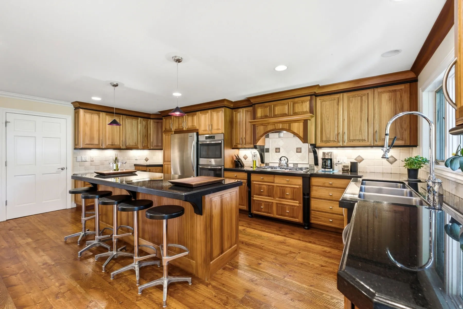 Kitchen featuring wood-finish flooring, recessed lighting, wood cabinetry, built-in stainless steel appliances, and a central island with a dark countertop