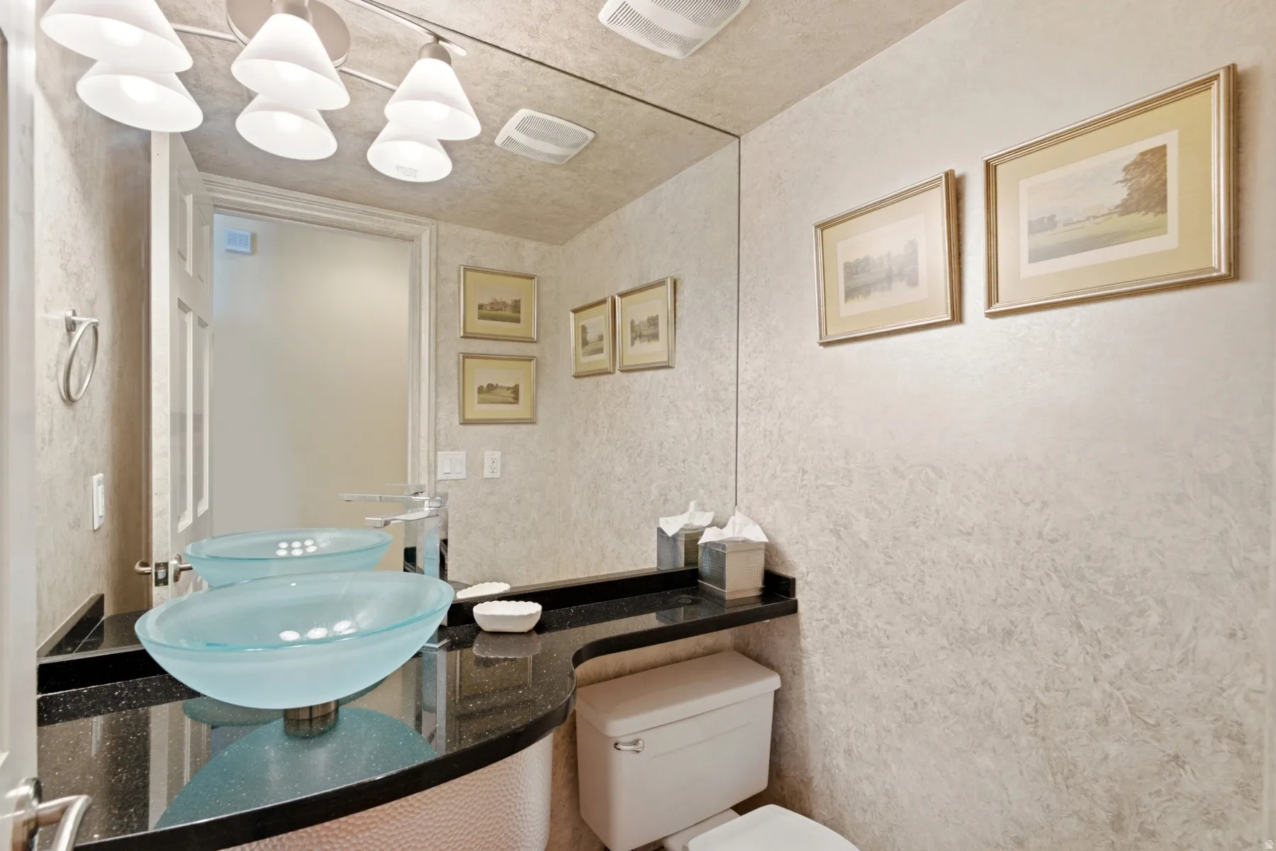 Vanity with dual vessel sinks, black countertop, wall-mounted faucet, and textured wall finish