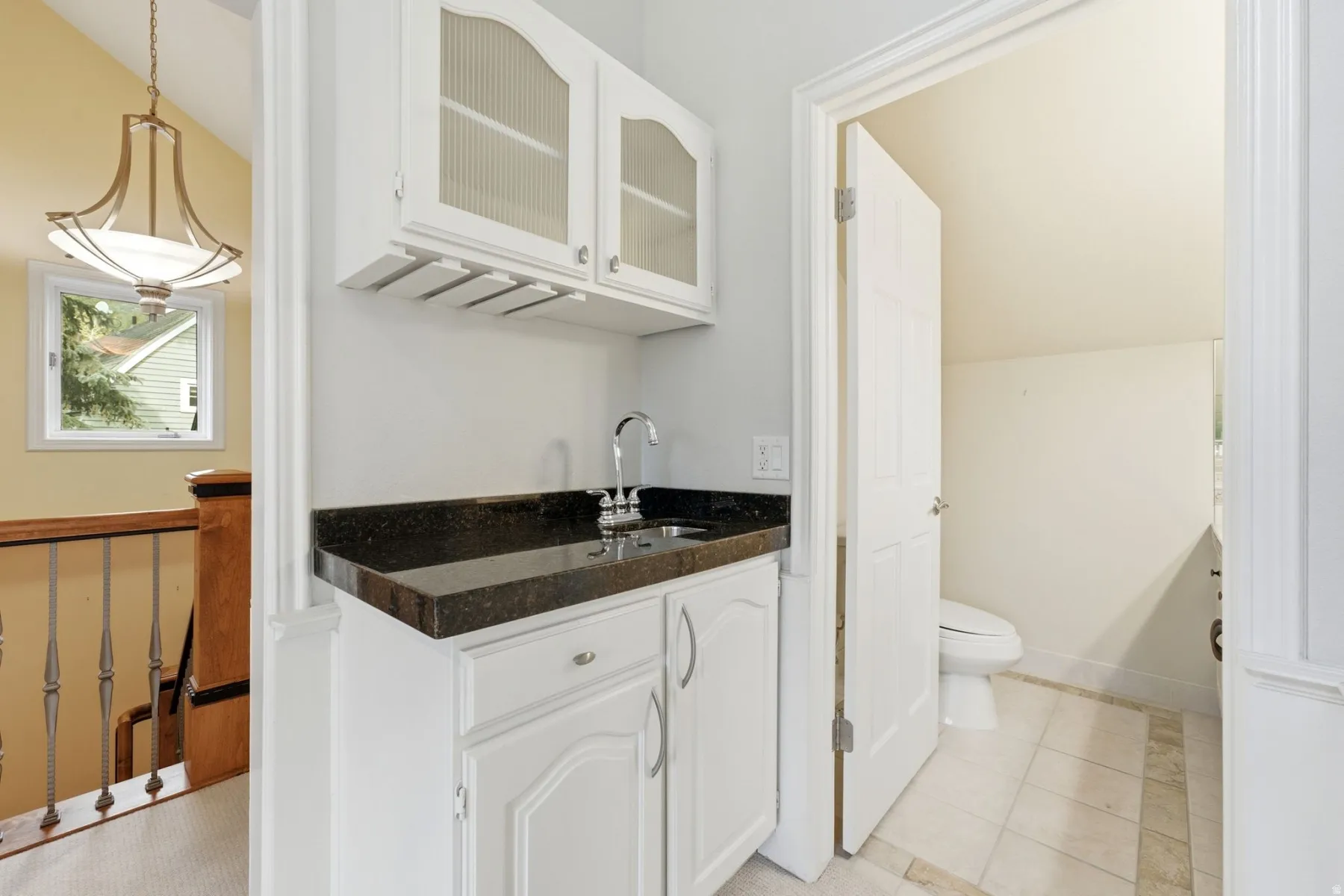 Built-in wet bar featuring a dark countertop, stainless steel sink, and upper cabinetry with reeded glass panels