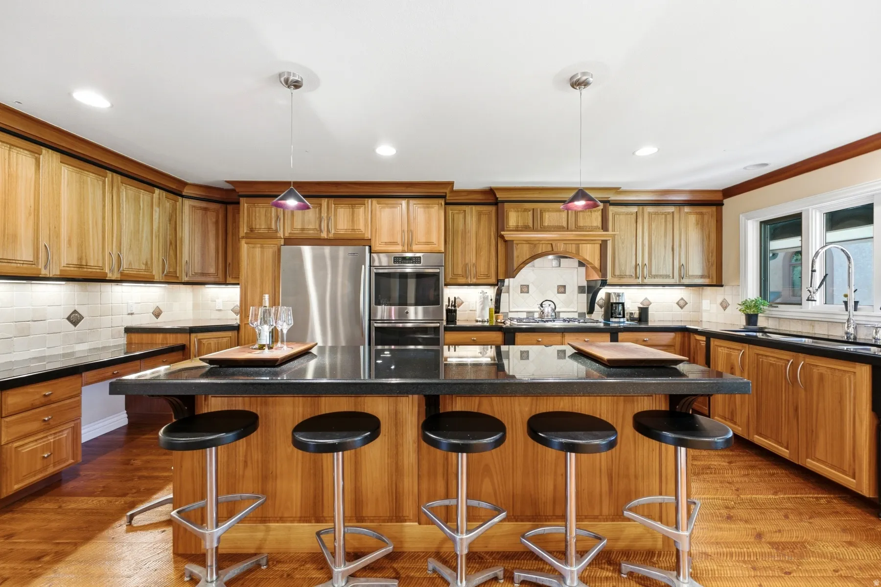 Spacious kitchen featuring wood-finish cabinetry, stainless steel appliances, a large center island with dark countertops, and wood-finish flooring