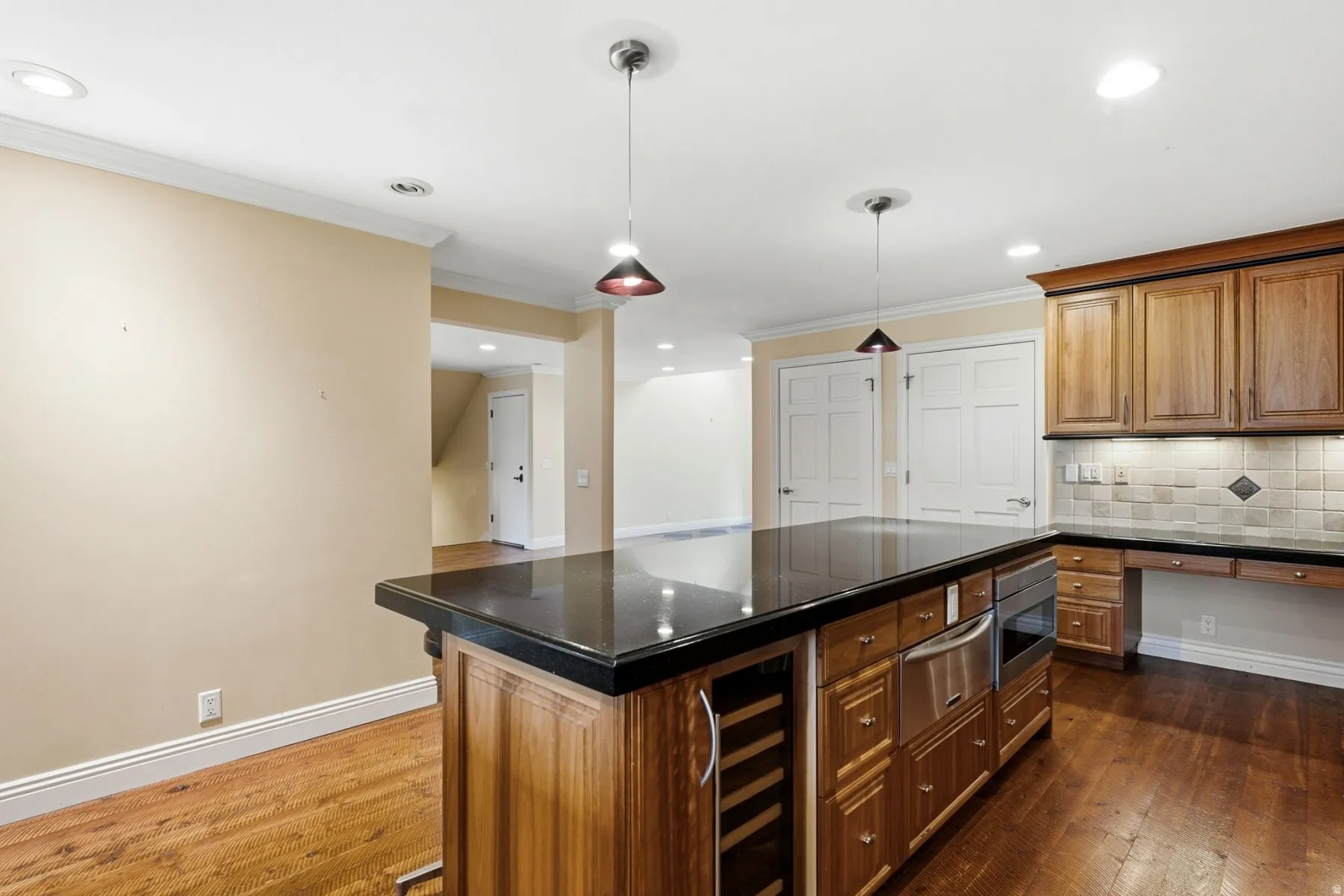 Spacious kitchen featuring a large island with dark countertop, wood-finish cabinetry, stainless steel appliances, and wood-finish flooring