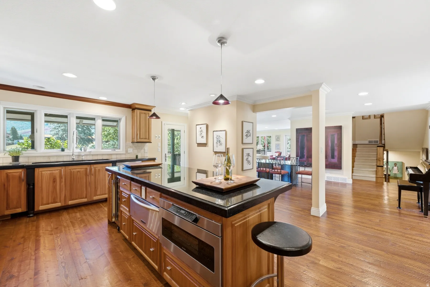 Hardwood flooring throughout, kitchen island with built-in microwave, integrated beverage cooler, and black countertop