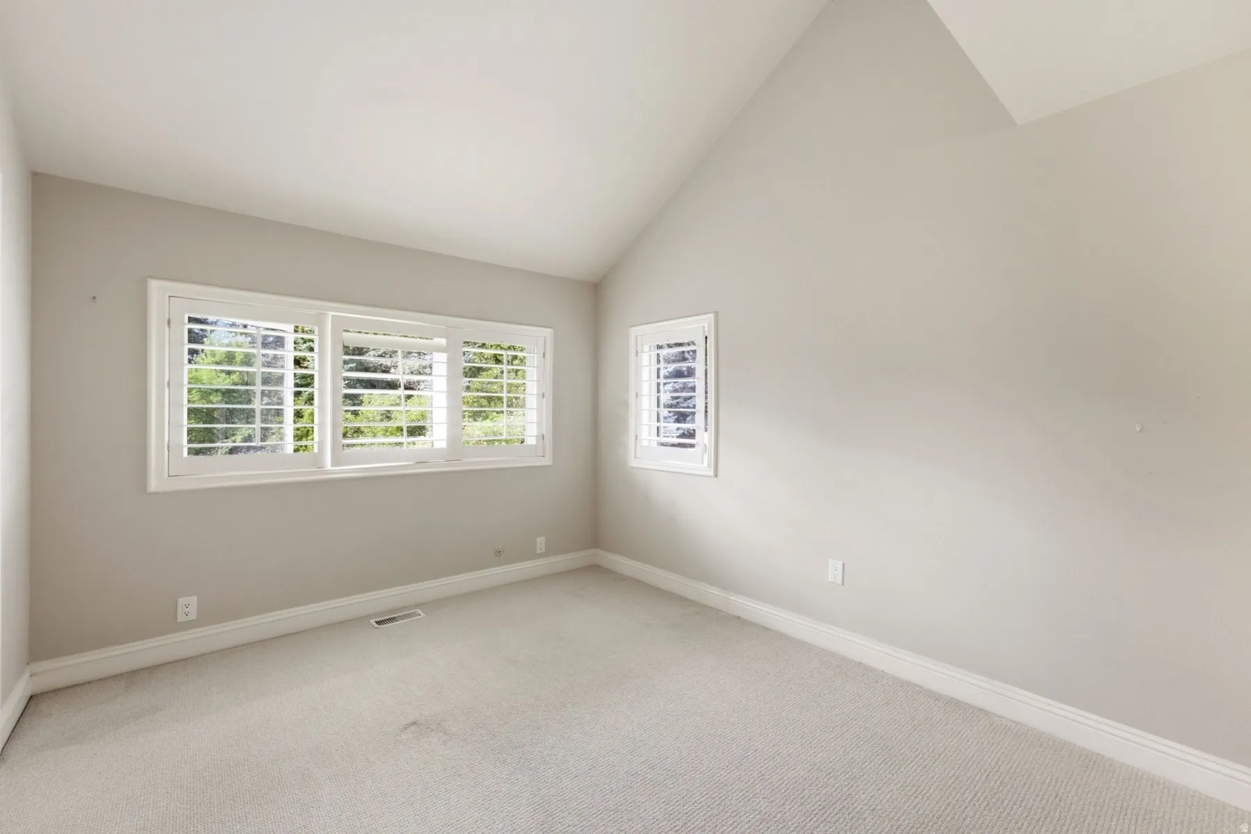 Vaulted ceiling with light-toned walls, featuring a wide window with plantation shutters, and a smaller window with plantation shutters
