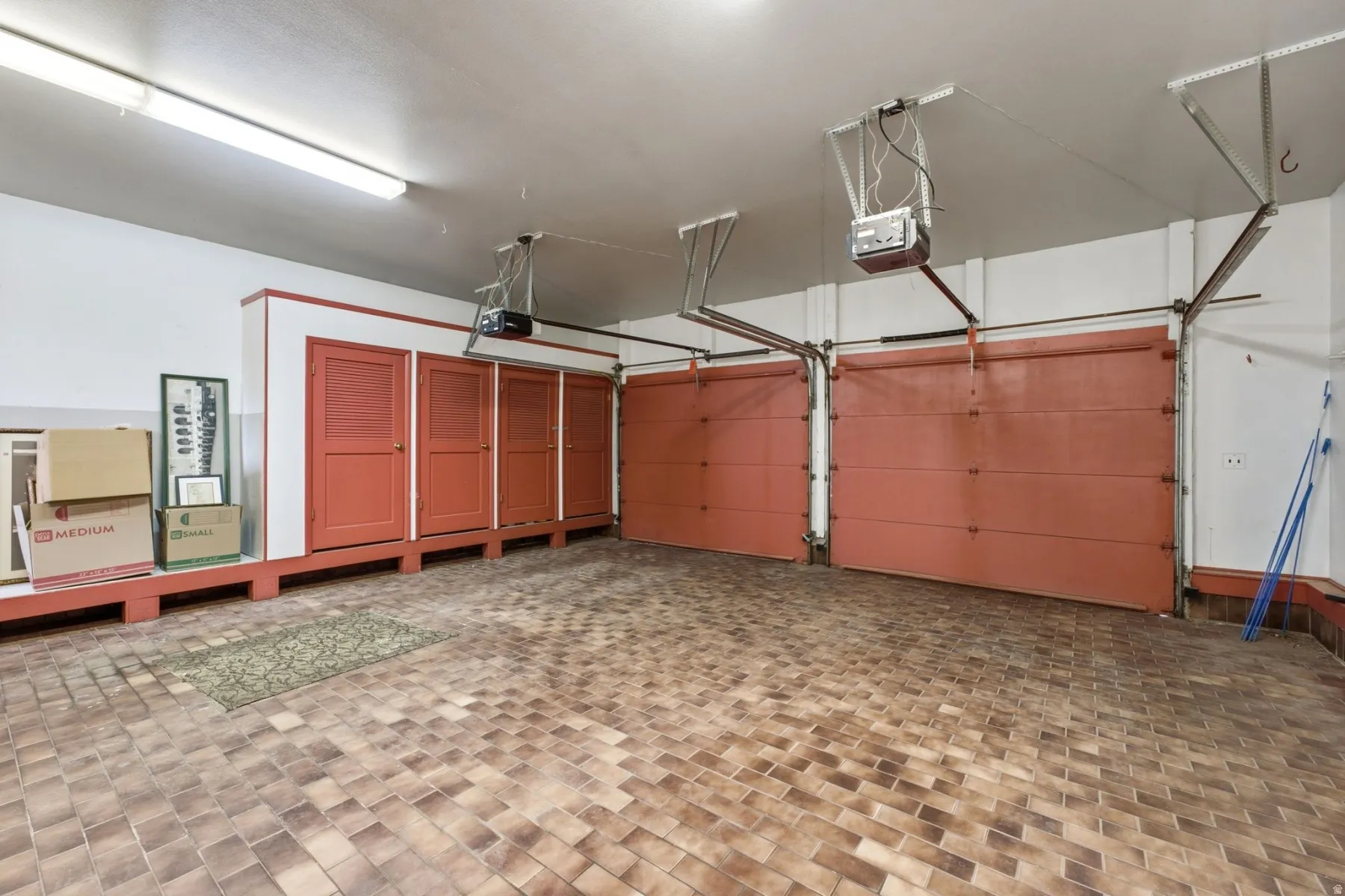 Two overhead garage doors with automatic openers, tile flooring, built-in cabinetry, and fluorescent ceiling lighting
