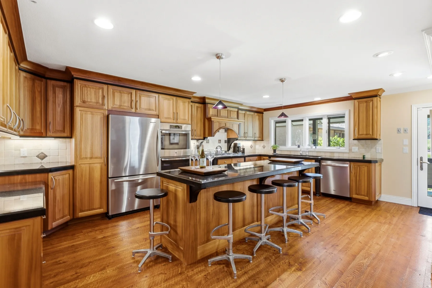 Expansive kitchen featuring wood-finish cabinetry, stainless steel appliances, a center island with seating, dark countertops, and wood-finish flooring