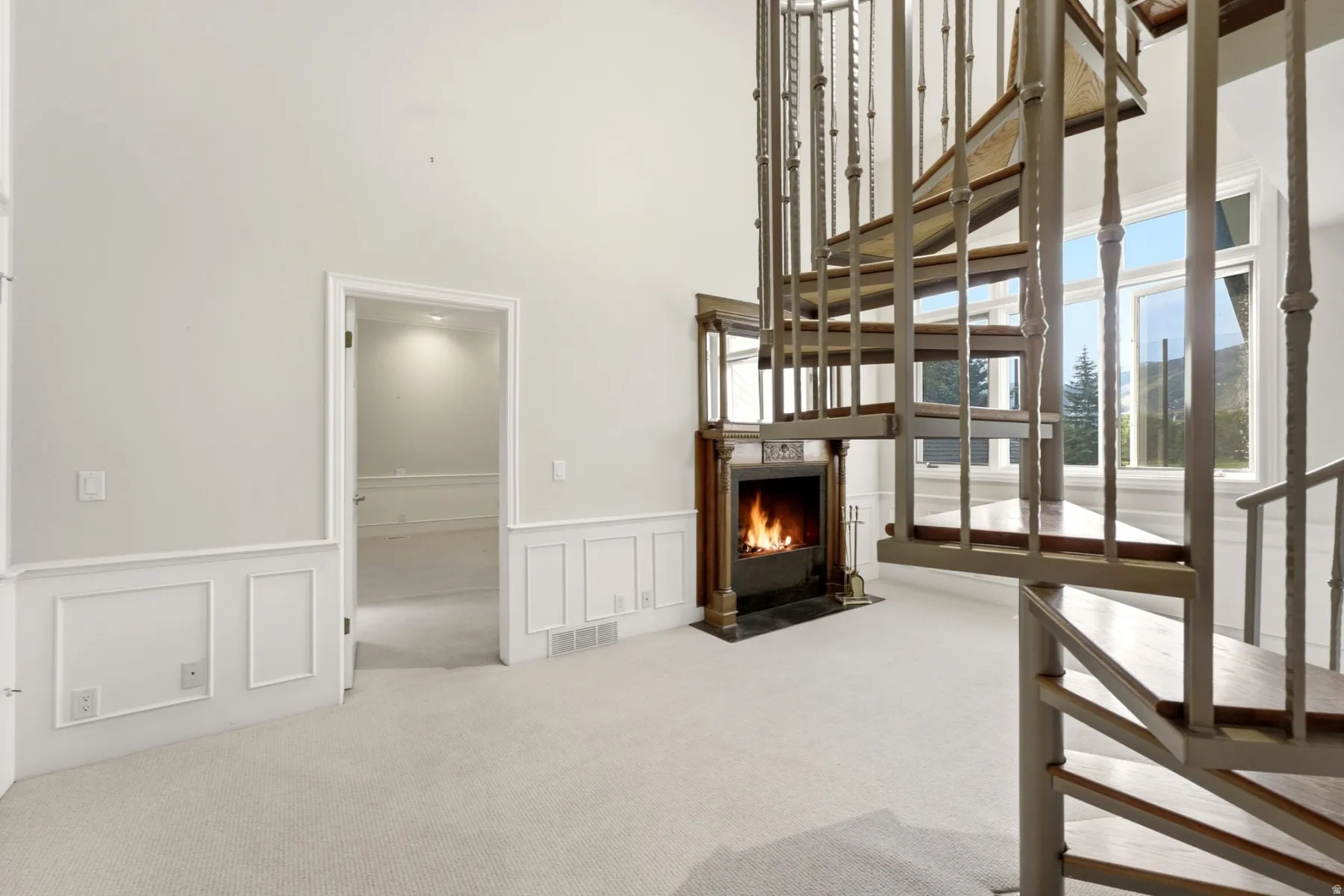 Spiral staircase with wood treads, fireplace with a decorative mantel, multiple windows, and wainscoting