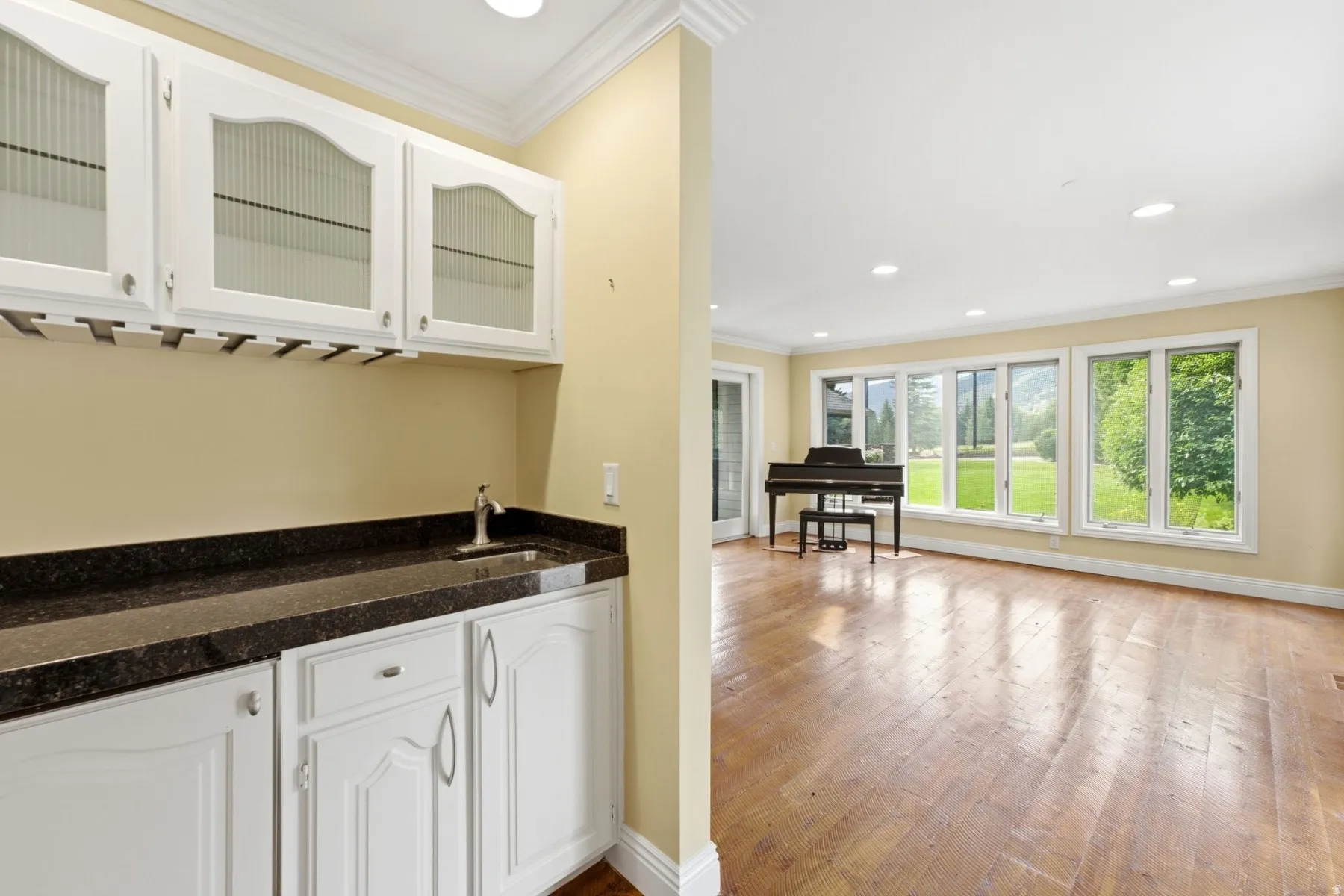Wet bar with white cabinetry and dark countertop, recessed lighting, expansive wood-finish flooring, and a wall of windows