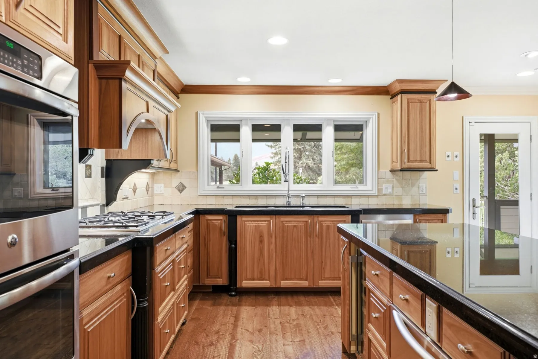 Kitchen featuring wood-finish cabinetry, stainless steel appliances, black countertops, and a tiled backsplash