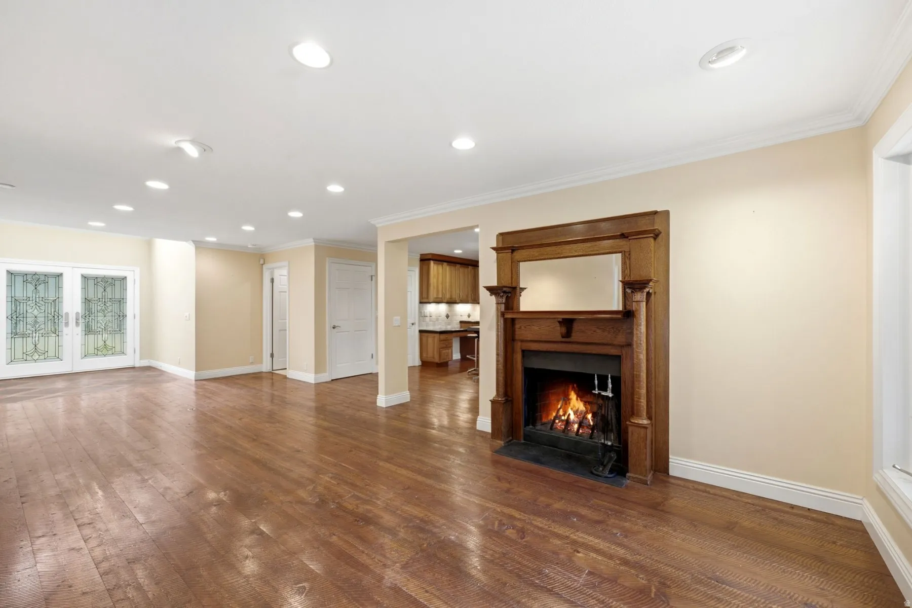 Hardwood flooring, recessed lighting, ornate fireplace with wood mantel, crown molding, and decorative glass double doors