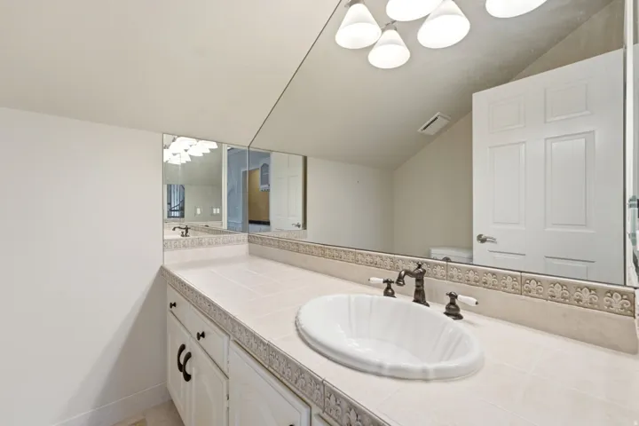 Spa-inspired bathroom vanity featuring dual sinks with white vessel basins, stone-finish countertops with decorative tile inlay, oil-rubbed bronze faucetry, and white cabinetry with hardware accents