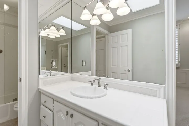 White vanity with integrated sink, chrome-finish faucet, mirror-front medicine cabinets, and overhead lighting