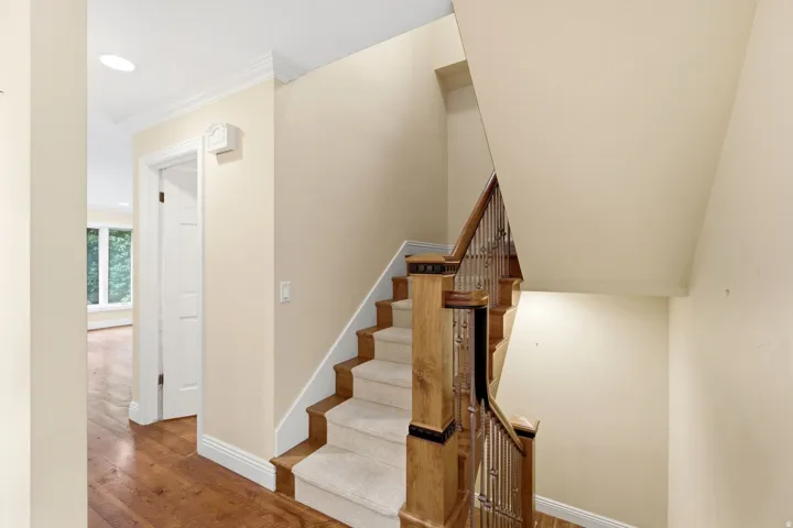 Staircase with wood treads and carpet runner, featuring wood newel posts and iron balusters