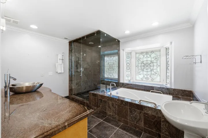 Walk-in shower with glass enclosure, built-in bathtub, ornamental stained glass window, and vessel sink with a stone countertop