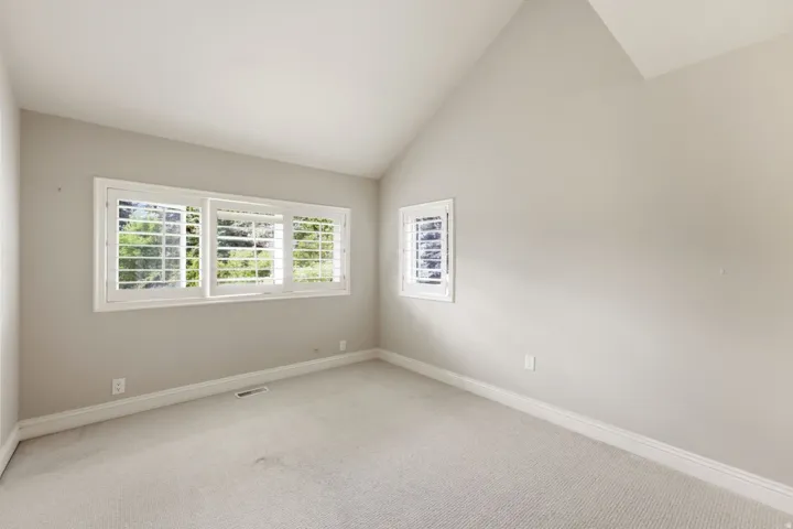 Vaulted ceiling with light-toned walls, featuring a wide window with plantation shutters, and a smaller window with plantation shutters