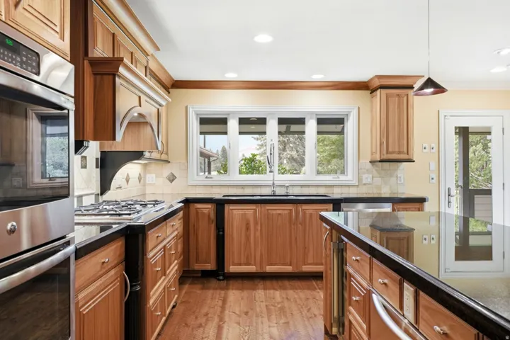 Kitchen featuring wood-finish cabinetry, stainless steel appliances, black countertops, and a tiled backsplash