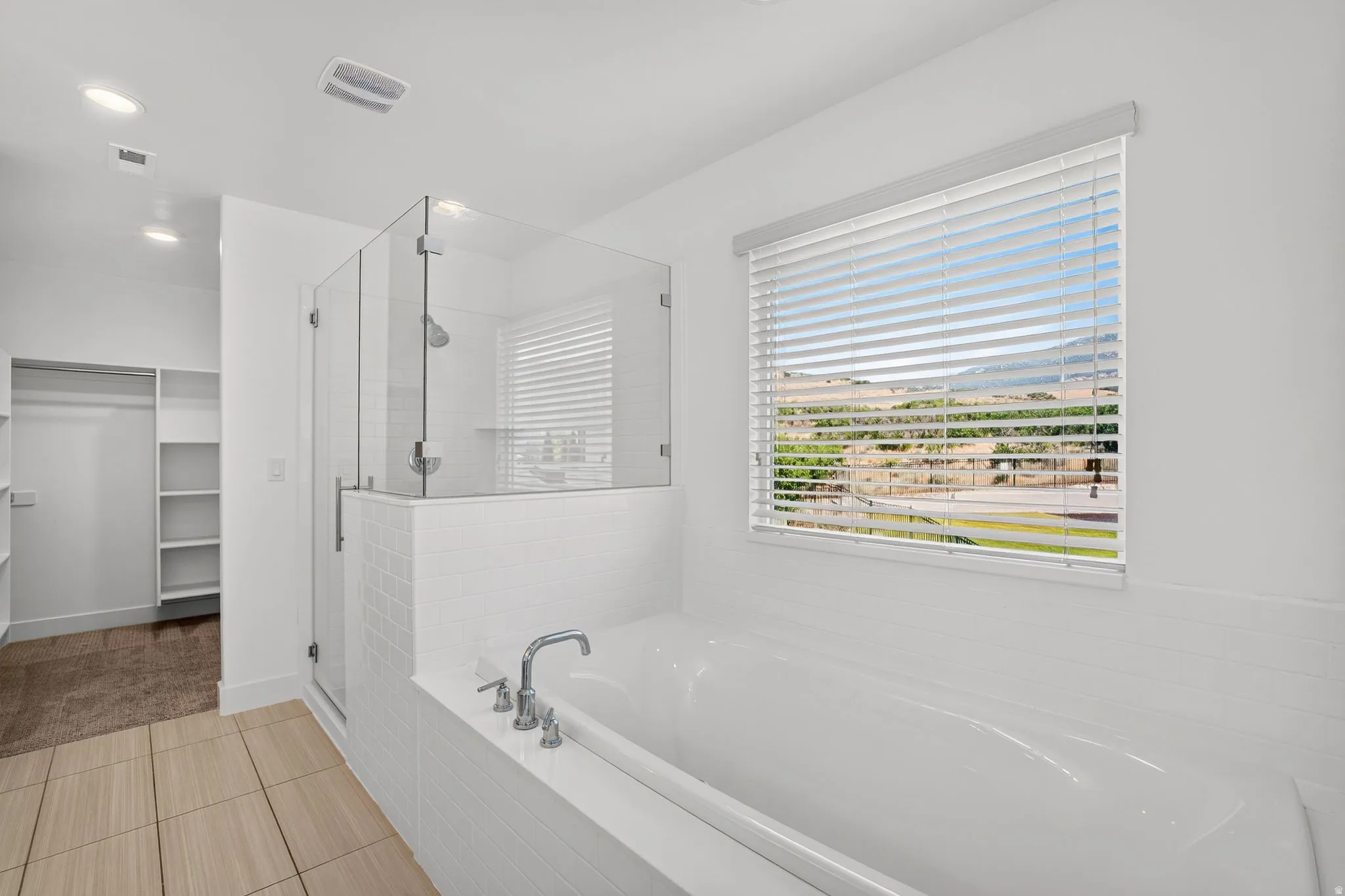 Contemporary bathroom featuring a built-in soaking tub with chrome fixtures, a glass-enclosed shower, white subway tile accents, and light-toned tile flooring
