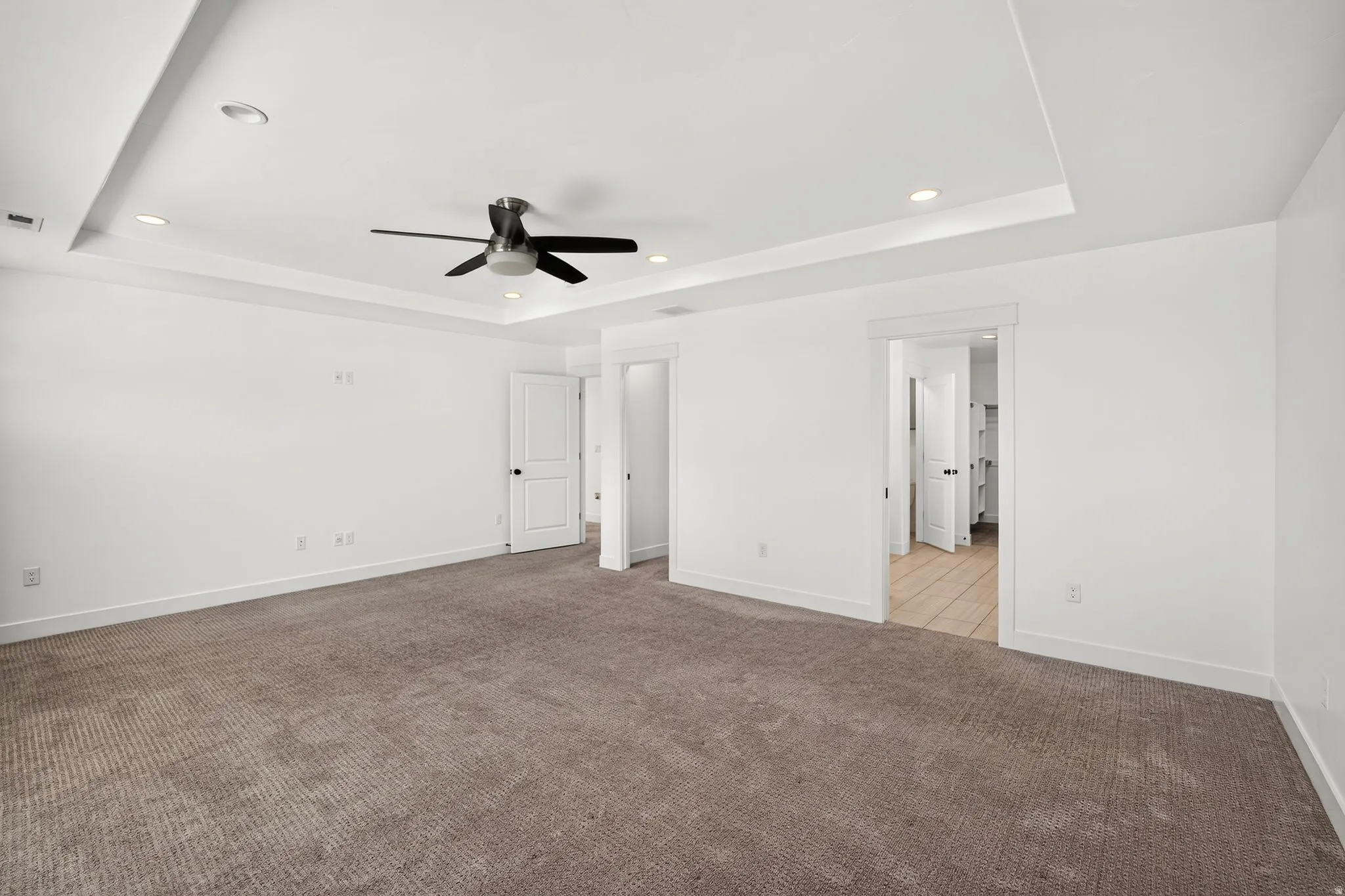 Spacious room featuring tray ceiling with recessed lighting, ceiling fan, carpet flooring, and white trim