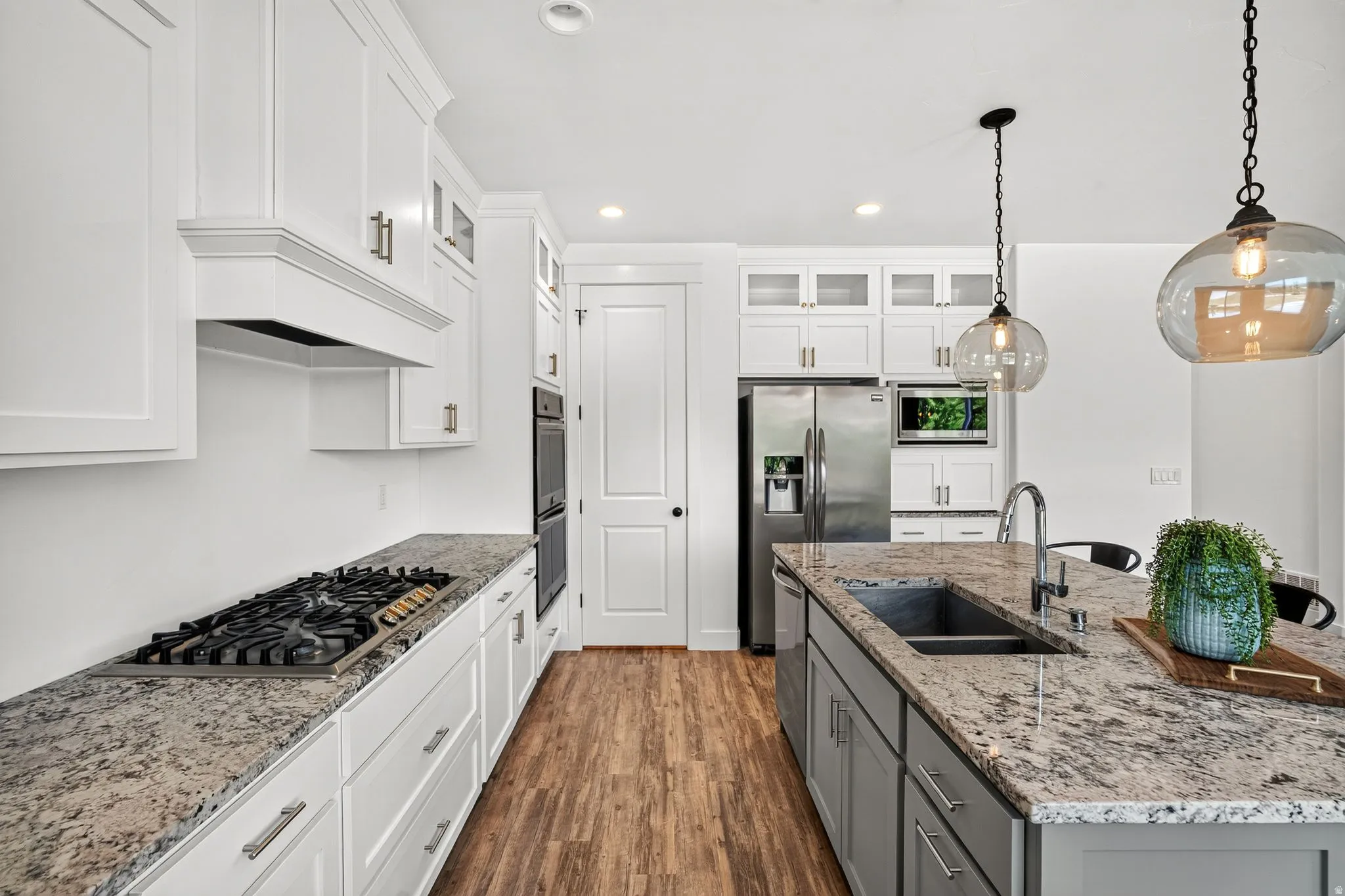 Modern kitchen featuring white cabinetry, granite countertops, a gas cooktop, stainless steel appliances, and wood-finish flooring