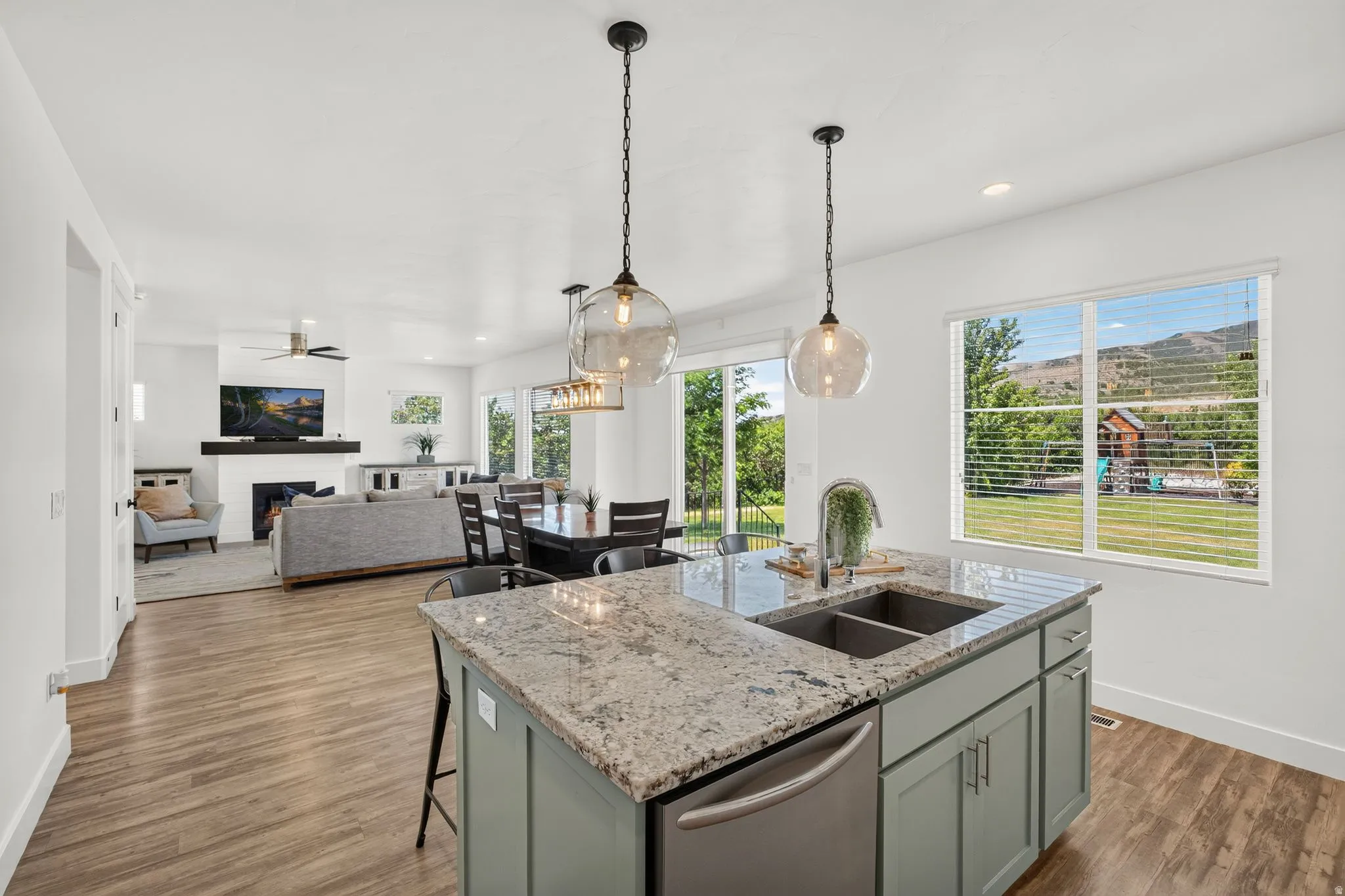 Kitchen island featuring a double basin sink, stainless steel dishwasher, light-colored granite countertop, and pendant lighting