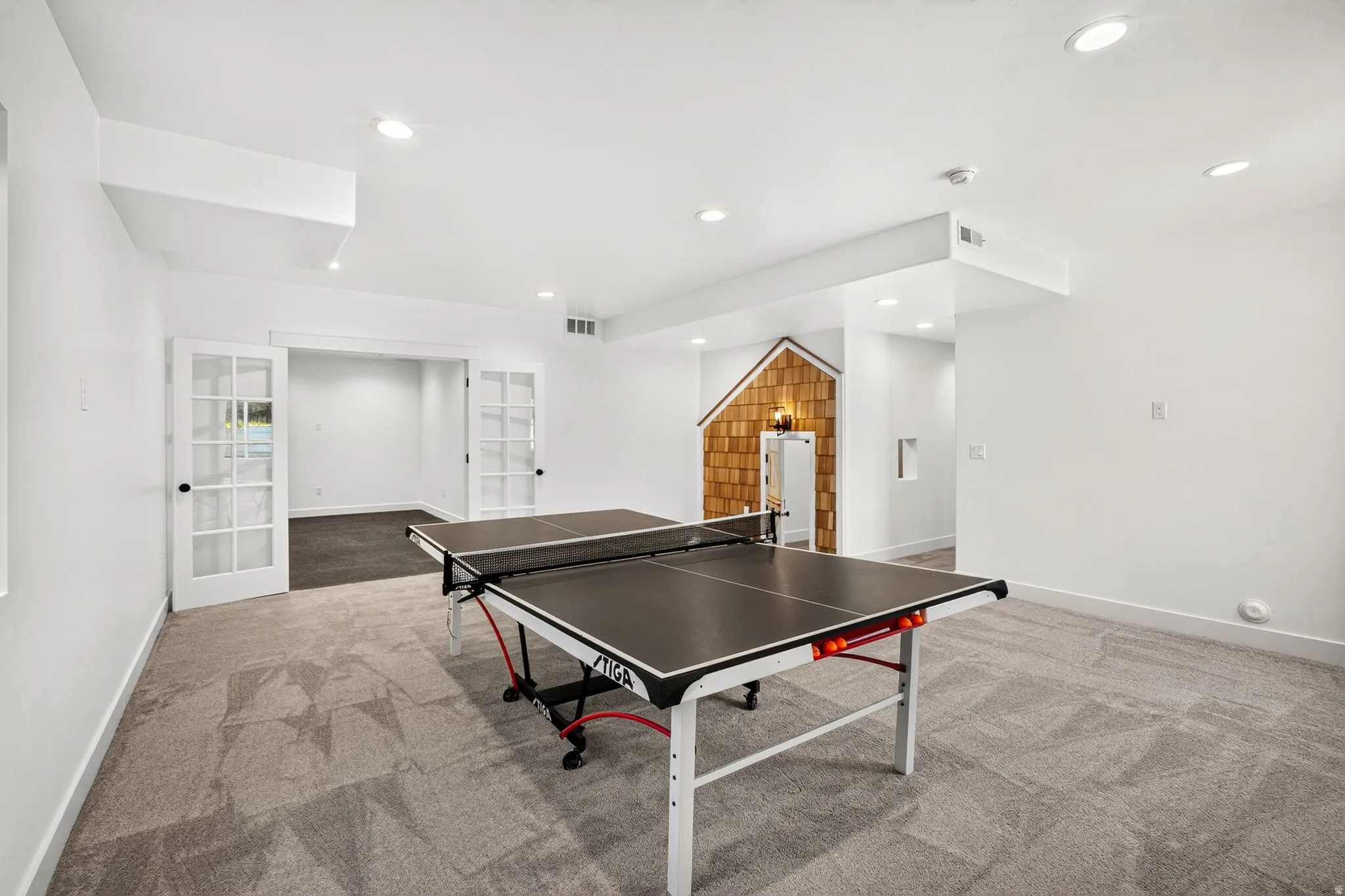 Spacious room featuring patterned carpeting, recessed lighting, white walls, and a separate room accessed by double French doors
