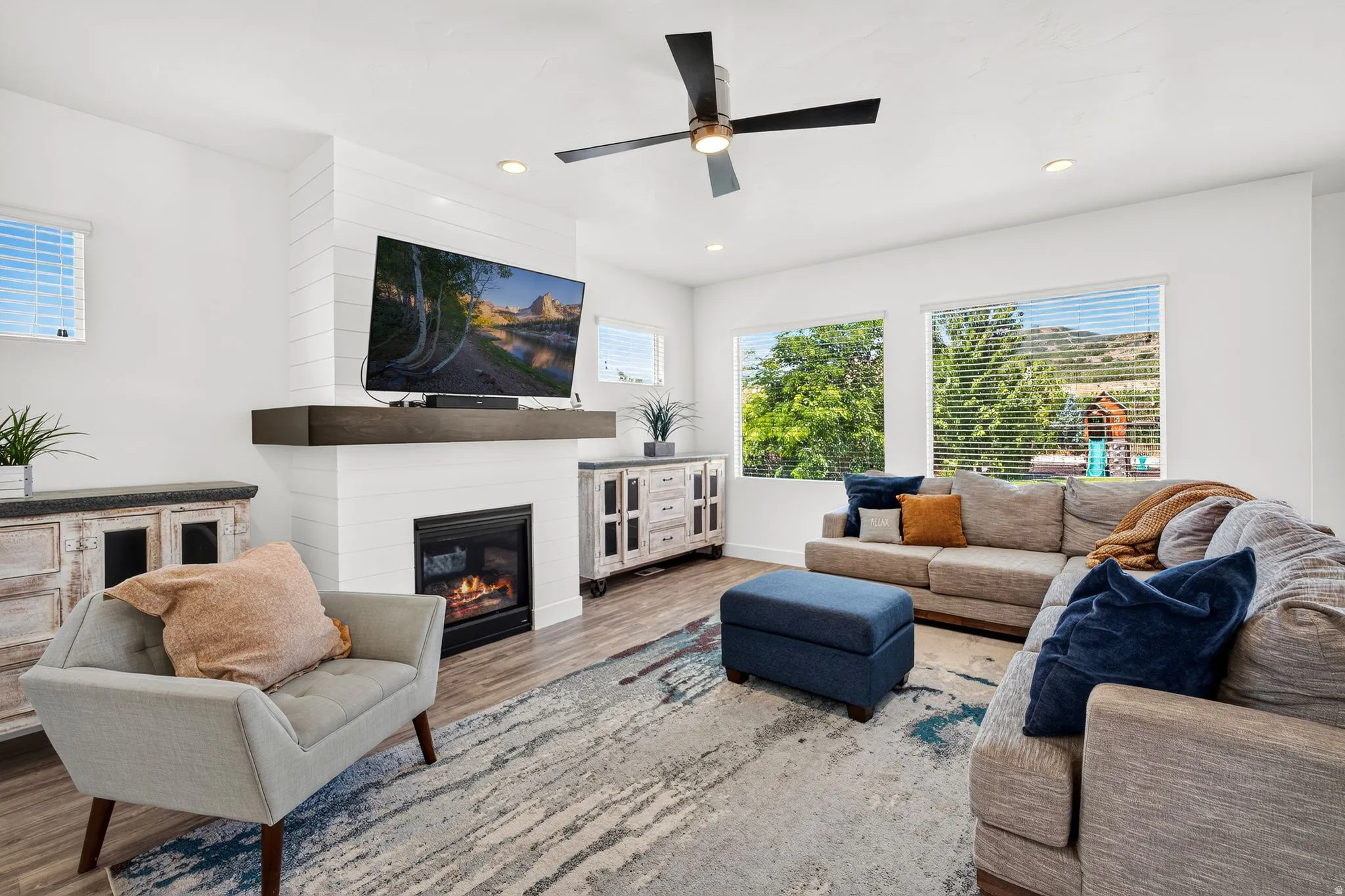 Living area featuring a shiplap-accented fireplace with a dark wood-finish mantel, recessed lighting, and a ceiling fan