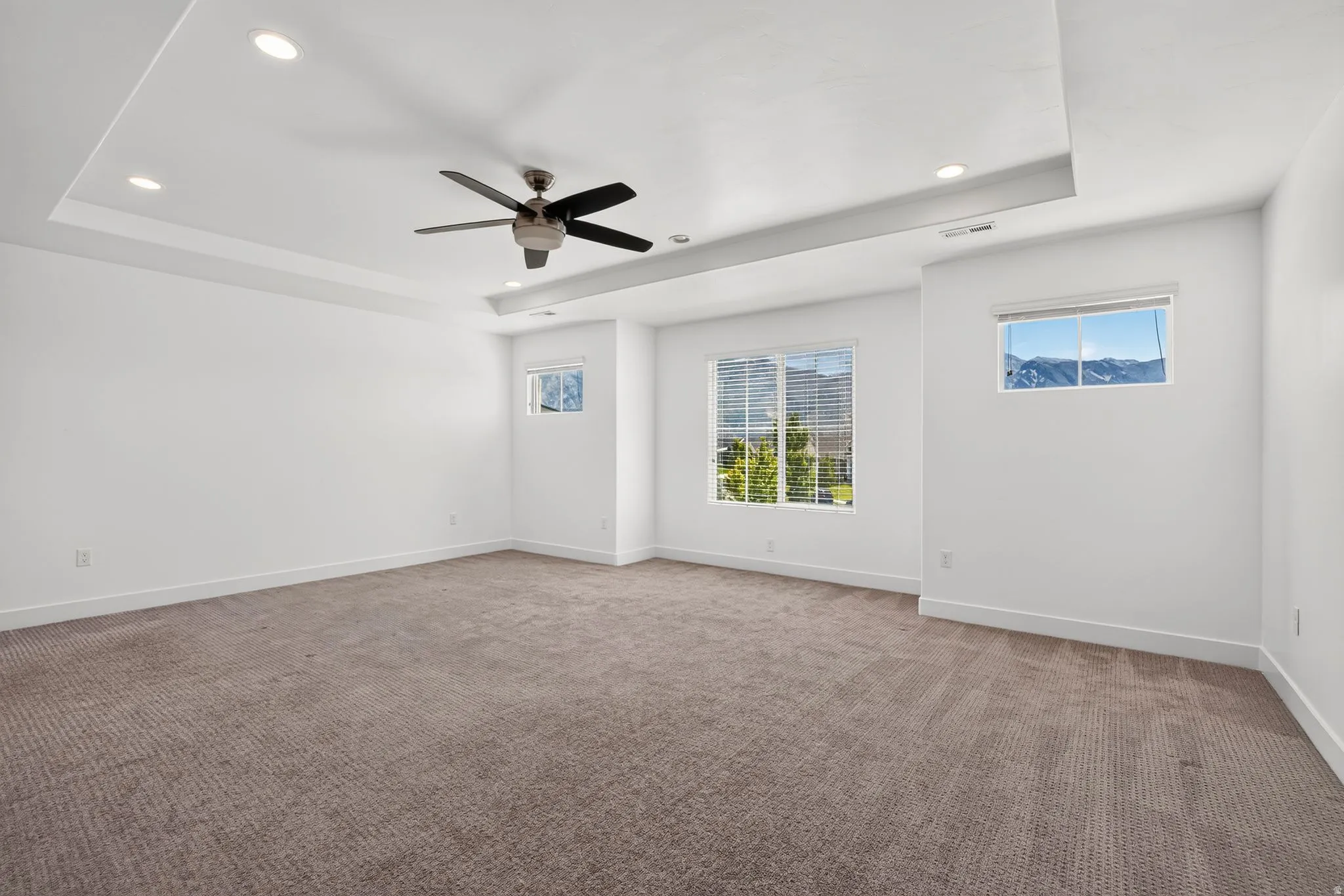 Spacious room featuring a tray ceiling with recessed lighting and a ceiling fan