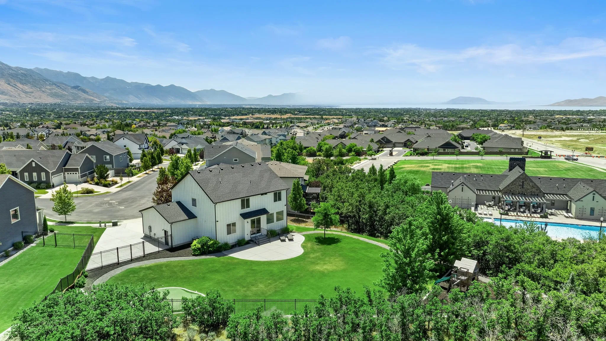 Aerial perspective showcasing a two-story residence with a white exterior, a sprawling green lawn, and a paved patio area