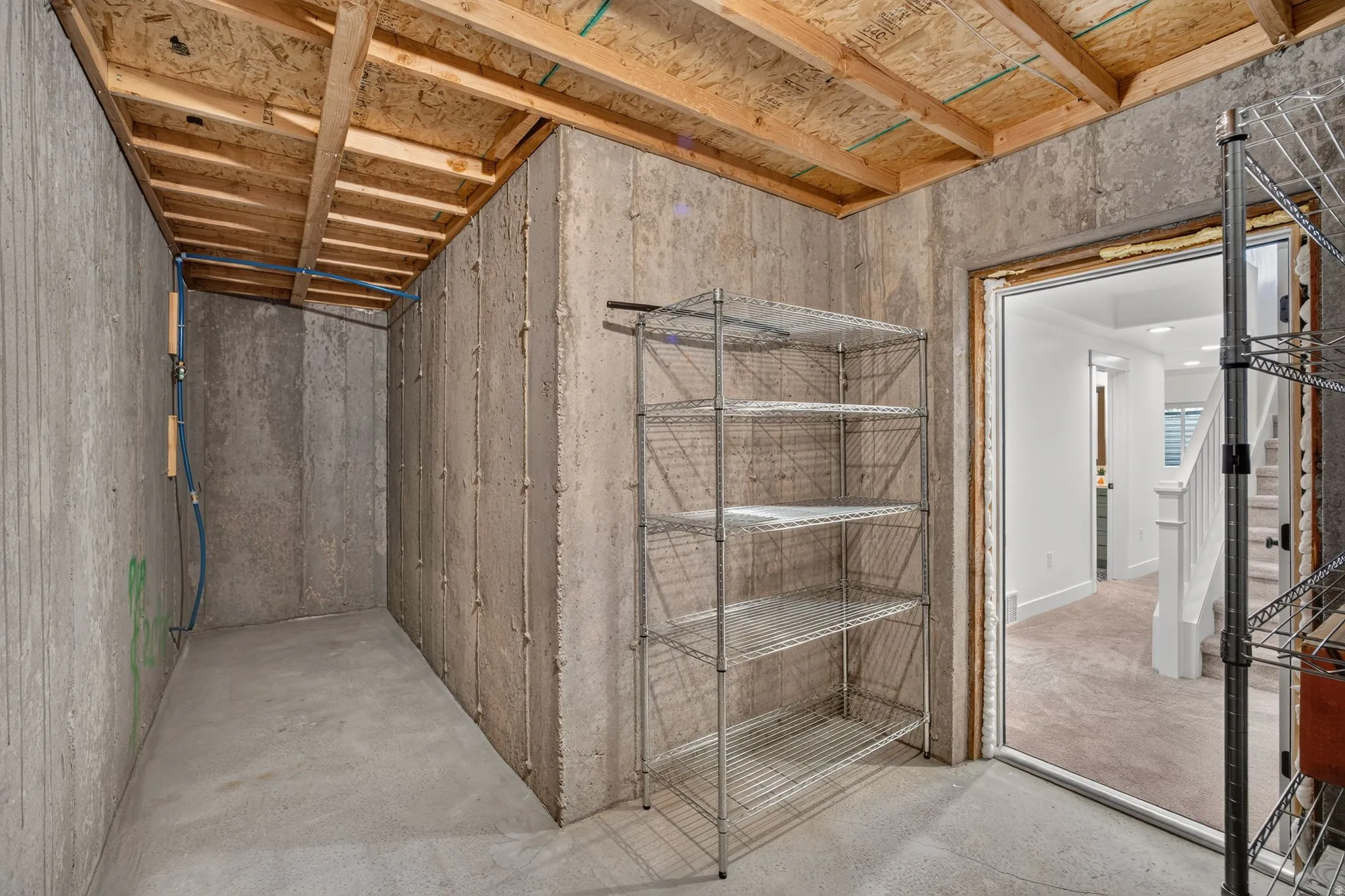 Unfinished basement area featuring concrete walls, concrete flooring, exposed wooden ceiling joists, and visible utility lines