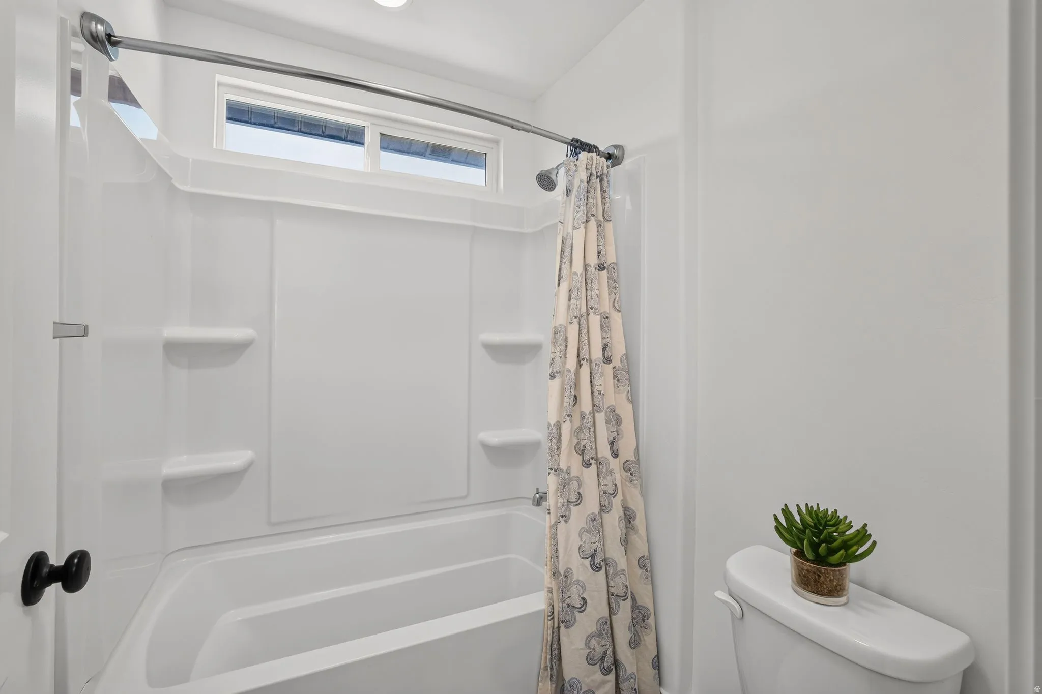 White bathtub and shower combination unit featuring an integrated soap dish and shelves