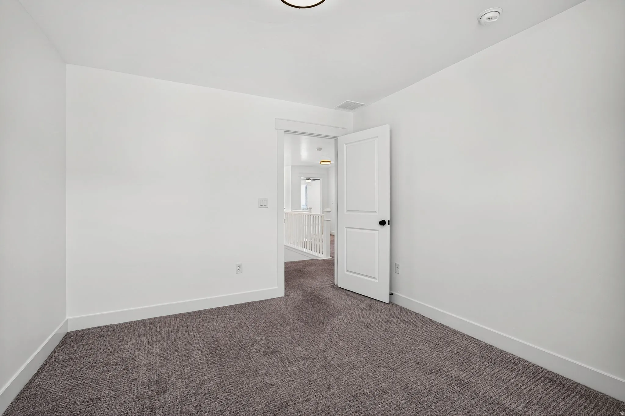 Bright room featuring white walls, deep gray carpeting, white baseboards, and a white interior door with black hardware