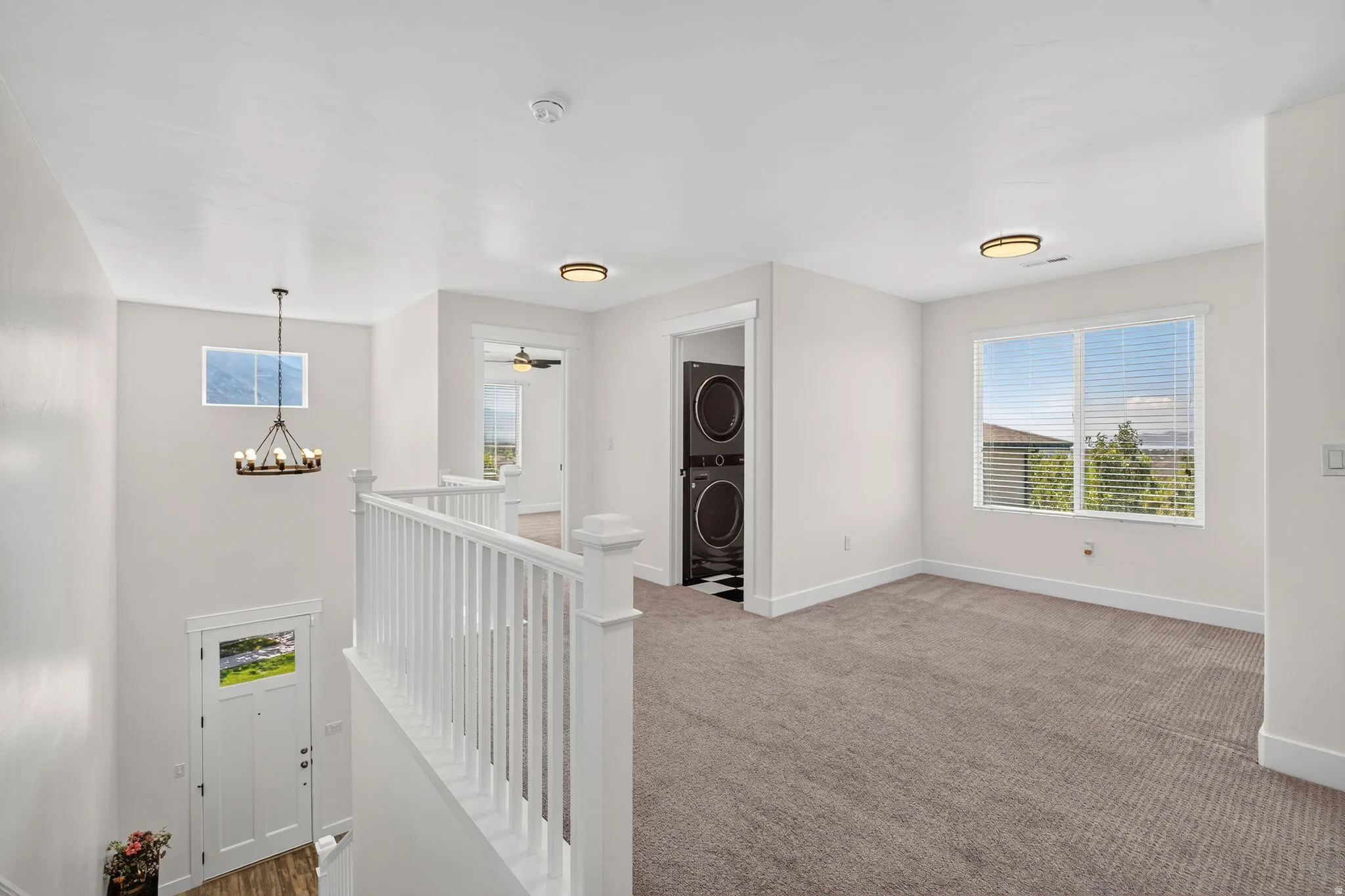Upper-level landing area featuring neutral carpeting, white balusters, and a contemporary chandelier