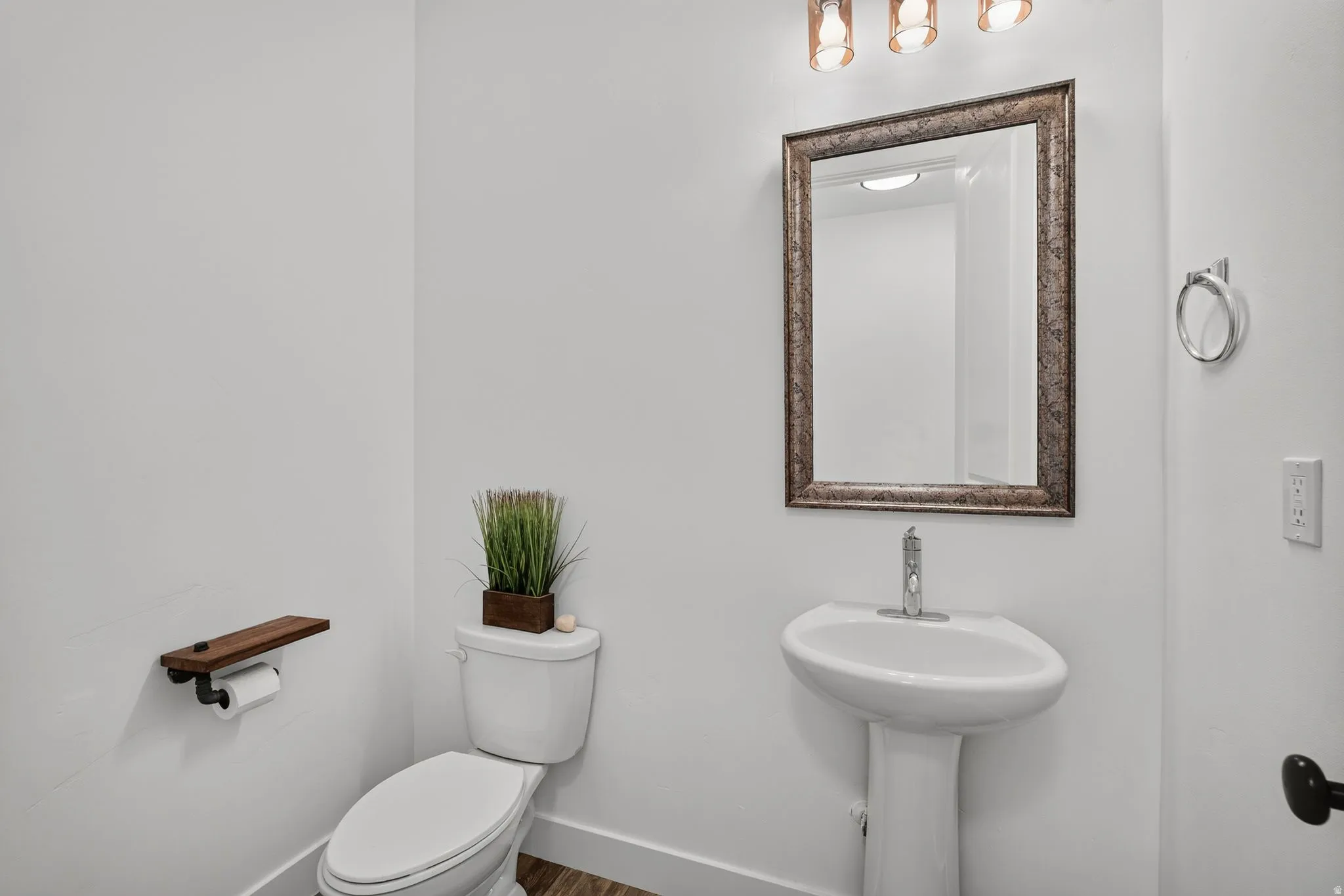 Pedestal sink with single-handle chrome faucet, framed mirror, and three-light vanity fixture