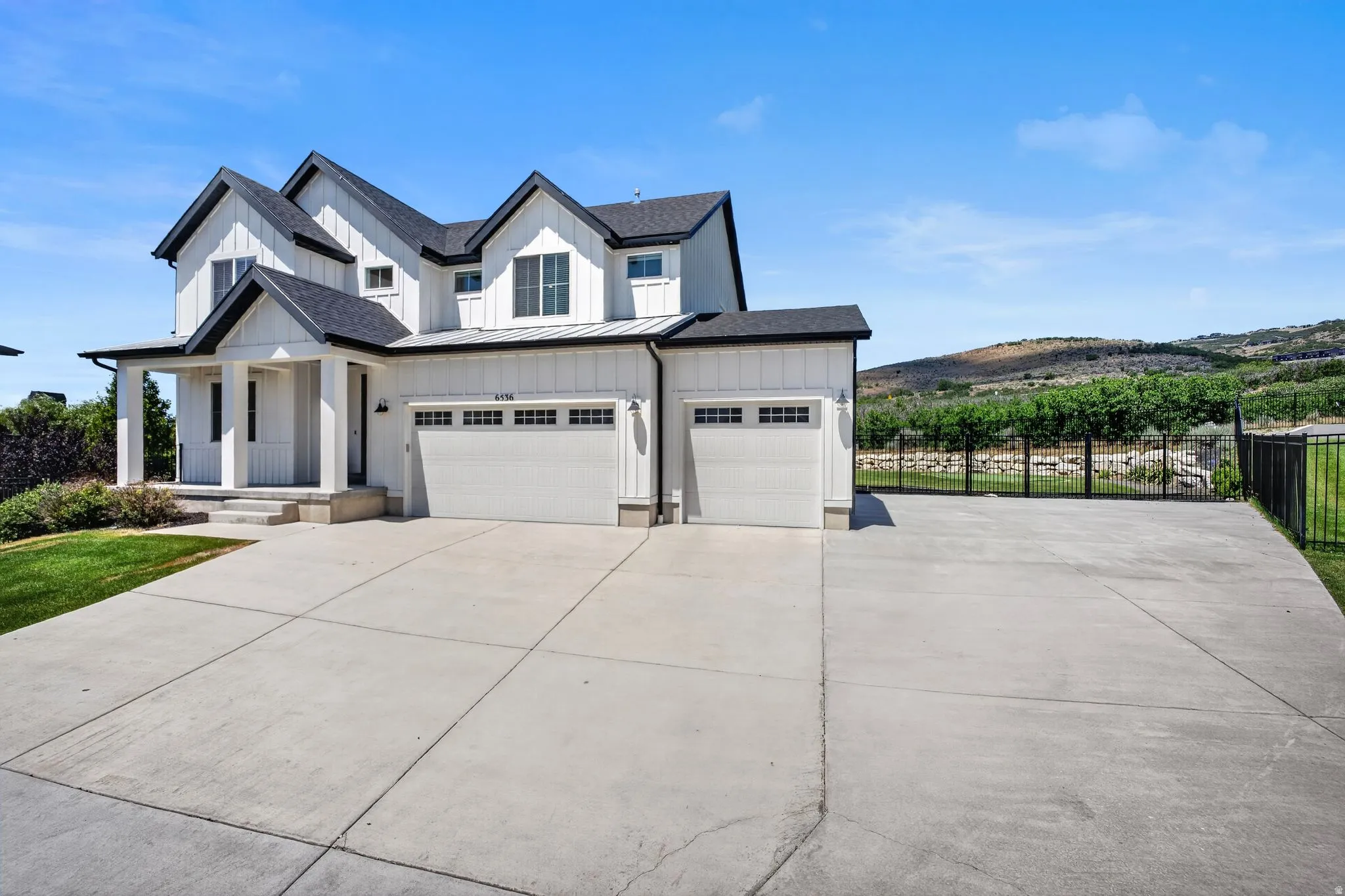 Modern farmhouse exterior featuring white board and batten siding, a prominent covered porch, and a multi-car concrete driveway