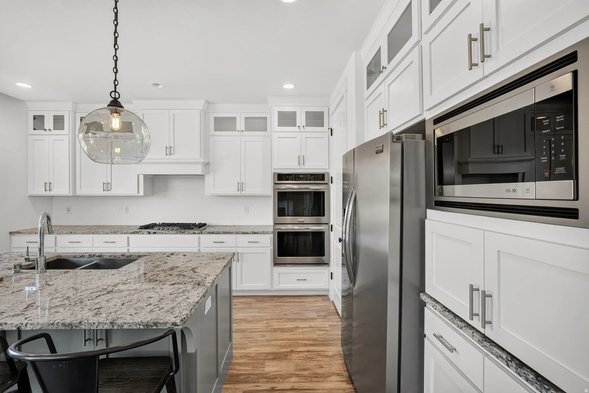 Gourmet kitchen featuring a large island with an undermount sink, white shaker cabinetry, stainless steel appliances, and wood-finish flooring
