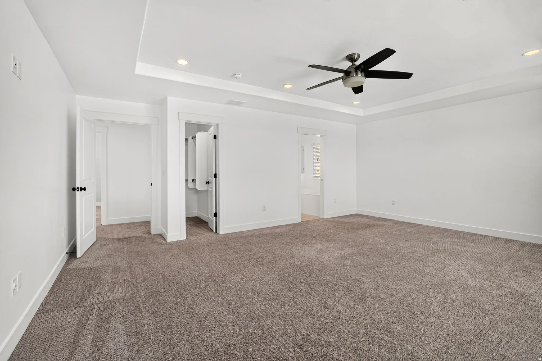 Spacious room featuring neutral carpeting, white walls, a tray ceiling with recessed lighting, and a ceiling fan