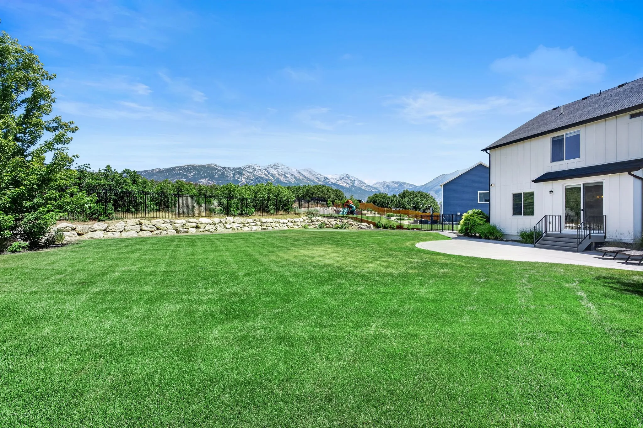 Expansive backyard featuring a manicured lawn, a large concrete patio, and a stone retaining wall