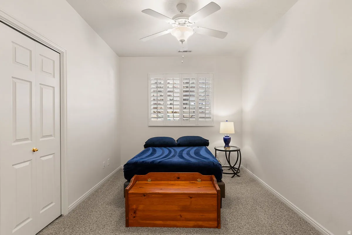 Room featuring a window with white louvered shutters, ceiling fan, carpet flooring, and white bi-fold closet doors