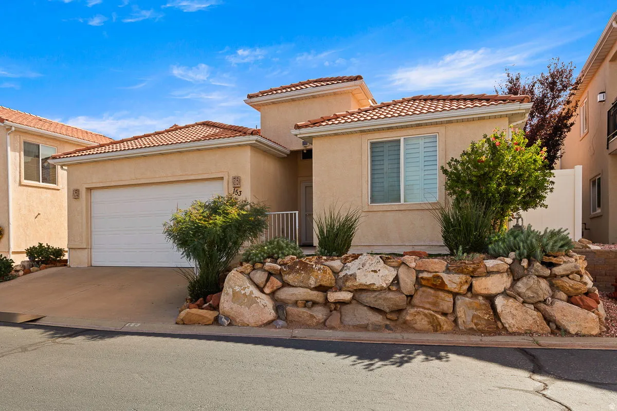 Stucco exterior with a tiled roof, integrated garage, and a decorative rock retaining wall